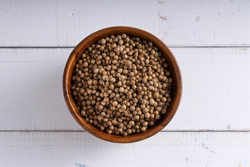 Uncooked red coriander seeds bowl. Studio shoot isolated on light wooden background. Up view shoot.