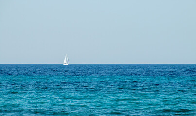 Velero navegando en el horizonte sobre un mar de aguas turquesas. Otranto, Italia. Velero en ruta por el canal de Otranto que conecta el mar Jónico y el mar Adriático. - obrazy, fototapety, plakaty