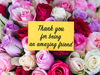 Yellow greeting card with words Thank You for Being an Amazing Friend laying on a big bouquet of colorful roses