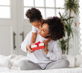 happy mother's day. african american baby daughter giving  gift box to her mom for holiday at home