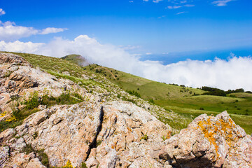 Stones and rocks of a mountain plateau in the foreground and green hills with stones and thorns in the background against a blue sky with voluminous clouds in summer in the Crimea in Ukraine.