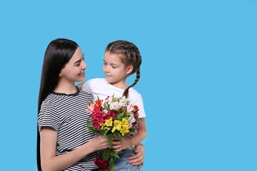 Fototapeta na wymiar Happy woman with her daughter and bouquet of beautiful flowers on light blue background, space for text. Mother's day celebration