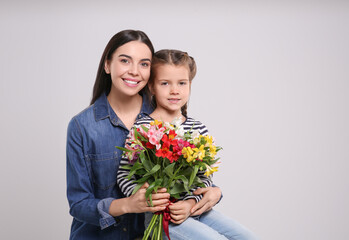 Happy woman with her cute daughter and bouquet of beautiful flowers on light grey background, space for text. Mother's day celebration