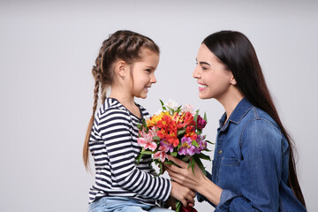 Happy woman with her cute daughter and bouquet of beautiful flowers on light grey background. Mother's day celebration
