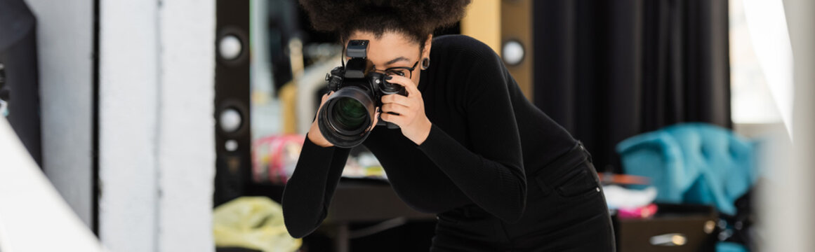 african american content producer in black turtleneck photographing on digital camera in photo studio, banner.