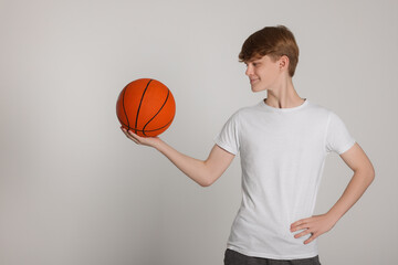 Teenage boy with basketball ball on light grey background. Space for text