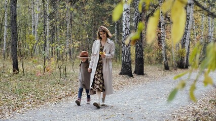 Hello September. A young mother and little daughter walk in the city park in autumn.