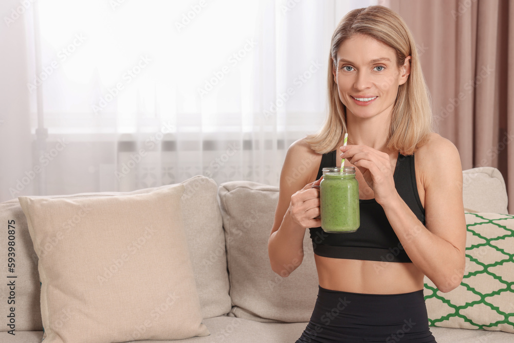 Poster Young woman in sportswear with mason jar of fresh smoothie at home, space for text