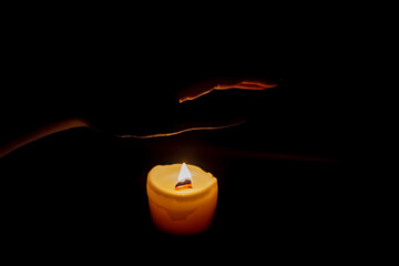 In the dark, a hand reaches for a flame candle. The warmth of the candle warms the skin. The faint...