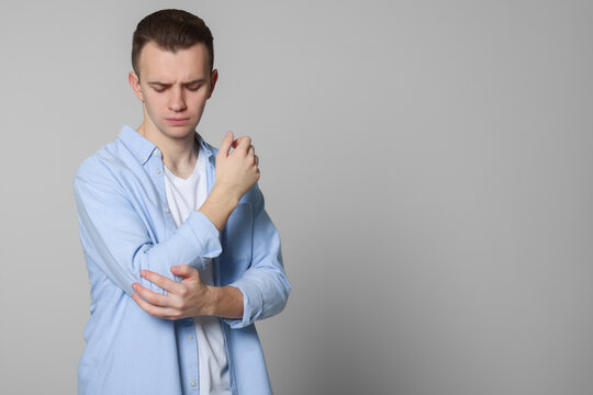 Young man suffering from pain in his elbow on light grey background, space for text. Arthritis symptoms