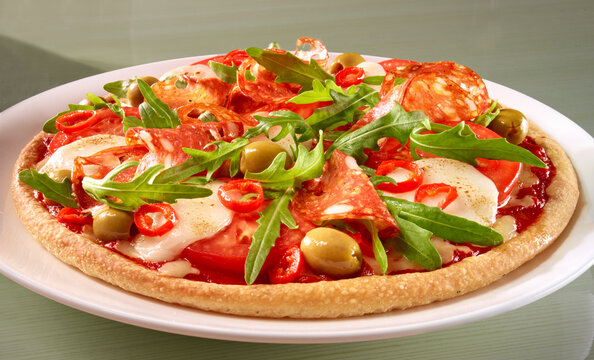 Pizza mit Tomaten und Rucola dazu grüne Oliven und Salami