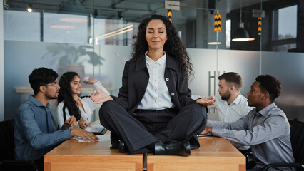 Calm businesswoman leader woman doing breathing yoga exercise taking break meditating sitting at...