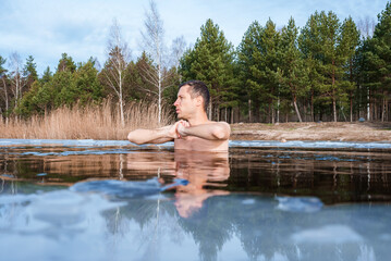 Man going ice swimming into a frozen lake during winter. Man standing between the ice pieces and meditating.