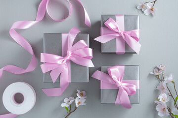 Silver gray gift boxes with pink satin bows on a gray background. Surprise present.