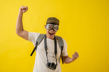 Portrait of happy Asian traveler tourist man with retro camera and goggles isolated on yellow background.