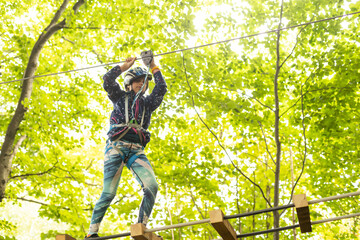 Little girl preschooler wearing full climbing harness having fun time in the rope park using carabiner and other safety equipment. Summer camp activity for kids. Adventure park in the forest