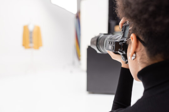 african american photographer taking photo on professional digital camera in blurred photo studio.