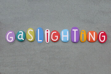 Gaslighting, psychological manipulation composed with multi colored stone letters over green sand