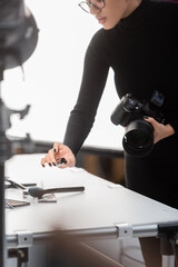 partial view of african american content producer with digital camera and mascara near decorative cosmetics on shooting table in photo studio.
