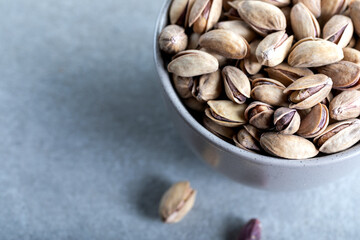 Bowl with pistachios on a grey concrete background. Green salted pistachios in ceramic bowl. Copy space, top view.