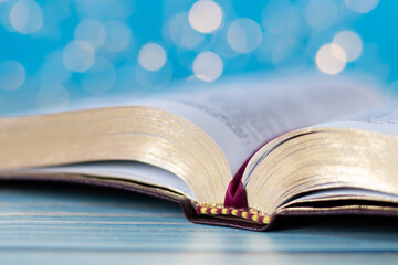 Open holy bible book with golden pages on wooden table with light blue bokeh background. A closeup. Studying Christian Scripture concept. Selective focus.