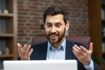 Successful smiling boss talking on video call, man in business suit inside office using laptop for online meeting, businessman joyfully talking and reporting.