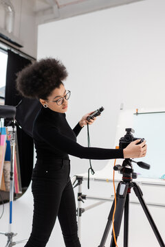 african american content producer with exposure meter adjusting digital camera in contemporary photo studio.