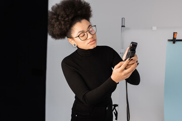 stylish african american content manager in black turtleneck looking at exposure meter in photo...