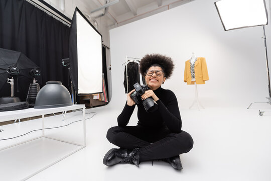 overjoyed african american content producer with digital camera sitting with closed eyes in modern photo studio.