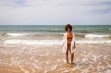 Young beautiful woman in bikini walking along the beach shore. The woman is enjoying her trip to a paradise beach while making different gestures and expressions. Holidays and travels.