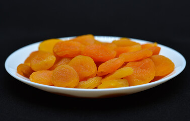 Dried fruits on a white plate. Dried apricot fruit halves without pits close-up.