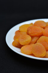 Dried fruits on a white plate. Dried apricot fruit halves without pits close-up.