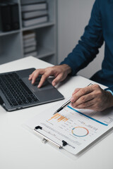 Fototapeta premium Close up view of young professional businessman analysis graph and chart while using laptop in the office room.