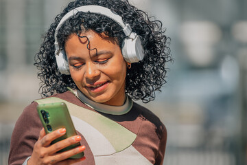 latin girl with afro hair with headphones and mobile phone in the street