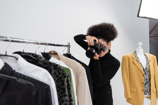african american photographer taking picture of fashionable clothes collection on rail rack in photo studio.
