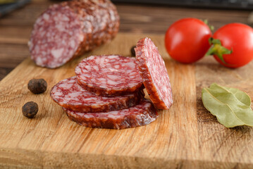 Salami sausage cut slices and salami sausage half with tomato, garlic, bay leaf and pepper on cutting board
