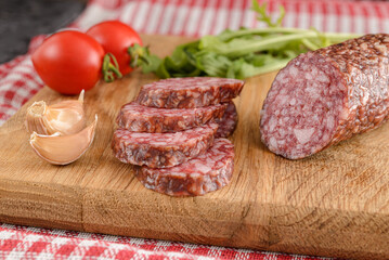 Salami sausage cut slices with tomato and garlic on wooden background