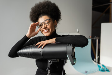 joyful african american content maker adjusting stylish eyeglasses and looking at camera near...