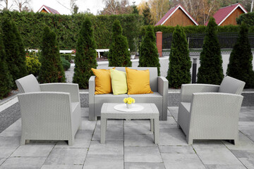 Beautiful rattan garden furniture, soft pillows and yellow chrysanthemum flowers in backyard