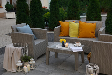 Beautiful rattan garden furniture, soft pillows and different decor elements in backyard