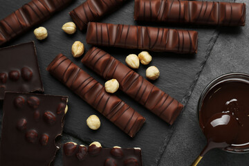 Tasty chocolate bars and nuts on black table, flat lay