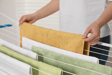 Woman hanging clean terry towels on drying rack indoors, closeup