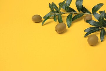 Fresh olives and green leaves on yellow background, closeup. Space for text