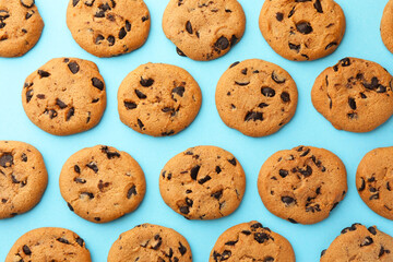 Many delicious chocolate chip cookies on light blue background, flat lay