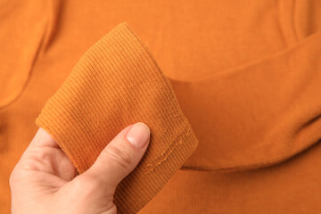 Woman holding sleeve of orange sweater with lint as background, top view. Before using fabric shaver