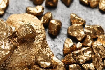 Pile of shiny gold nuggets on grey table, closeup