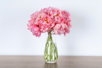 Beautiful bouquet of pink peonies in vase on wooden table against white background
