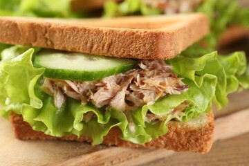 Delicious sandwich with tuna, cucumber and lettuce leaves on wooden board, closeup