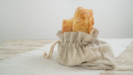 Artisanal ciabatta showcased in a sustainable linen bag, atop a wooden table adorned with a lovely tablecloth.