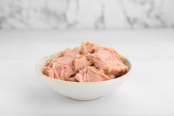 Bowl with canned tuna on white table, closeup